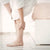 Femme en peignoir touchant ses jambes, illustrant un besoin de confort avec des chaussettes pour jambes sensibles.