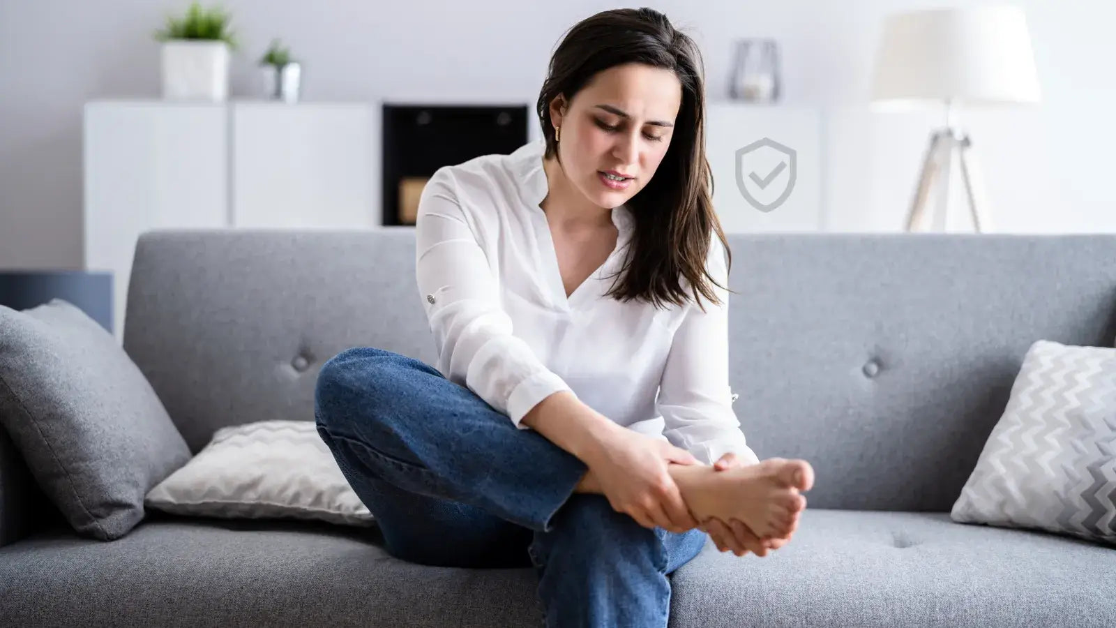Une jeune femme assise dans son canapé masse ses pieds pour soulager ses douleurs