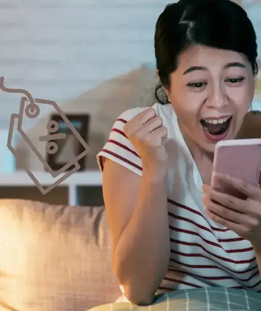 Femme heureuse de son achat en ligne qui manifeste sa joie avec le poing serré et le regard rivé sur son smartphone