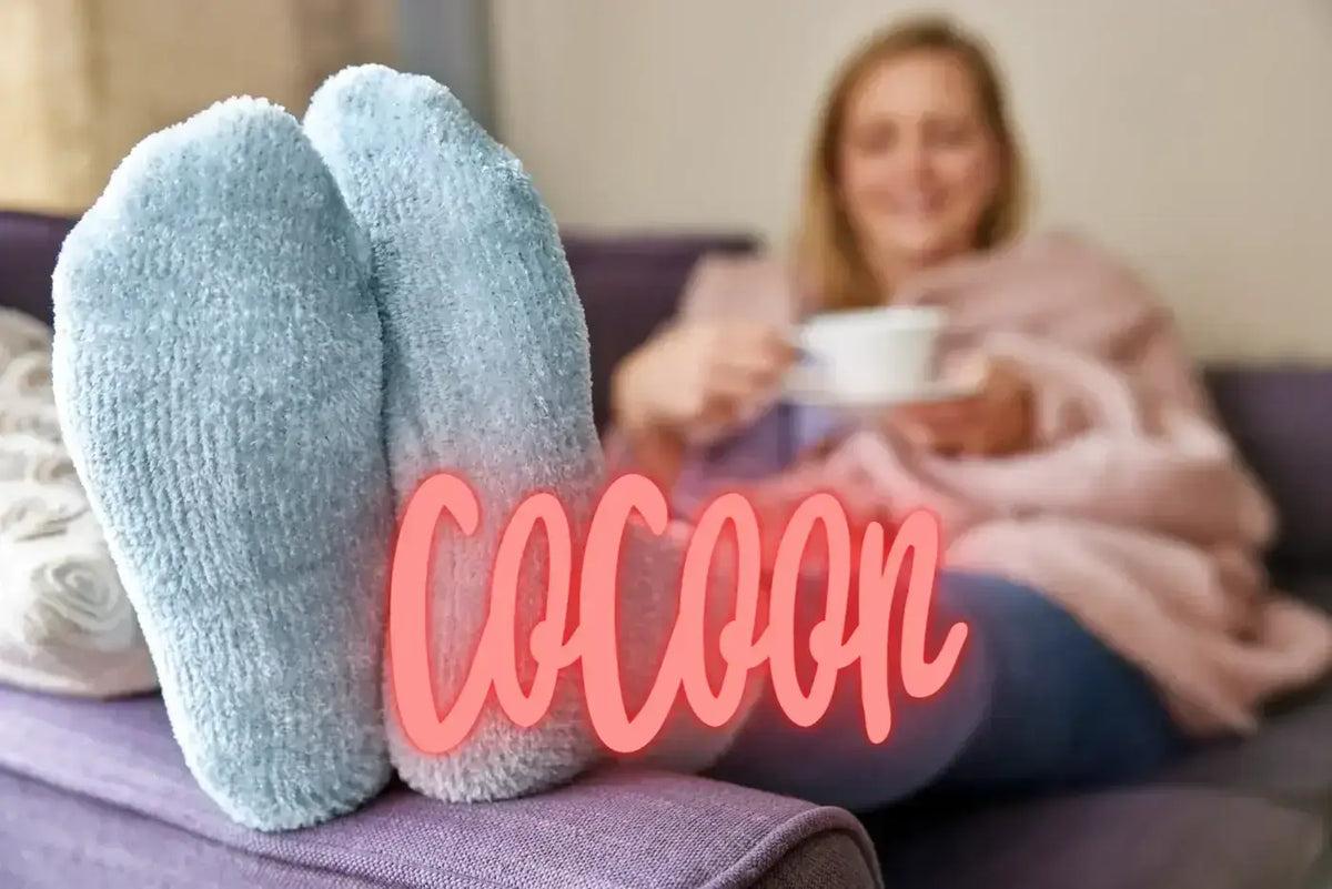 Femme avec des chaussettes polaires aux pieds dans son canapé à la maison dégustant une boisson chaude