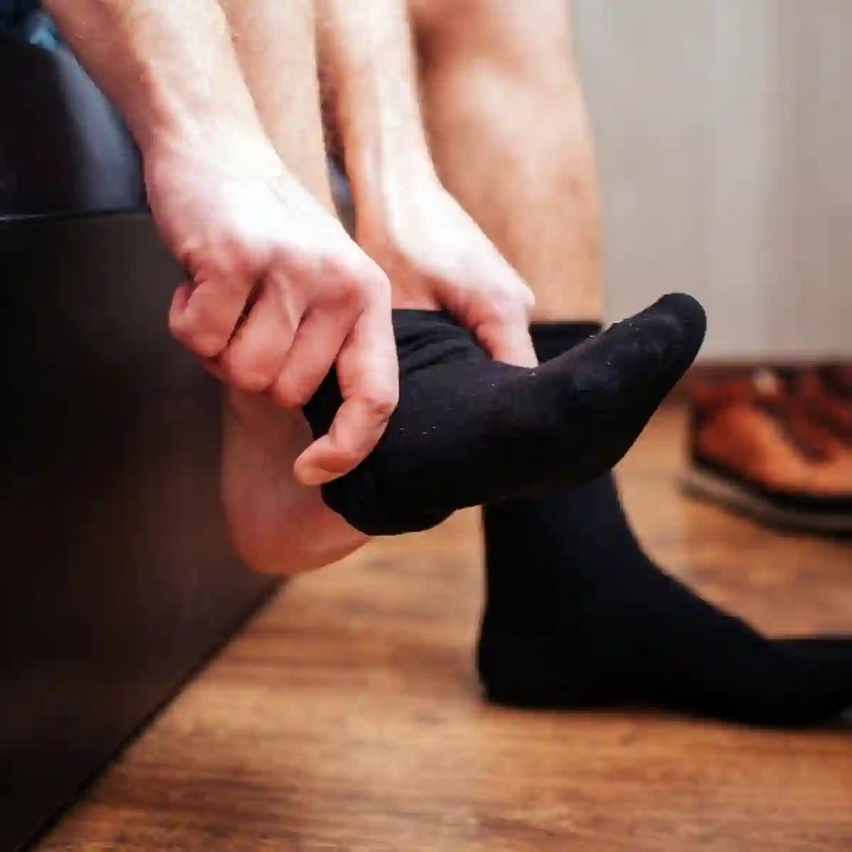 Homme enfilant des chaussettes faciles à enfiler noires sur un sol en bois.